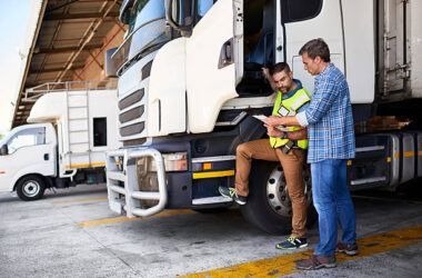 Shot of two coworkers talking together next to a large truck outside of a distribution center